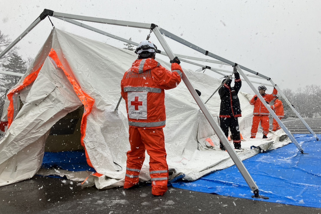 Staff members setting up a tent to accommodate first-aid workers in the snow.png