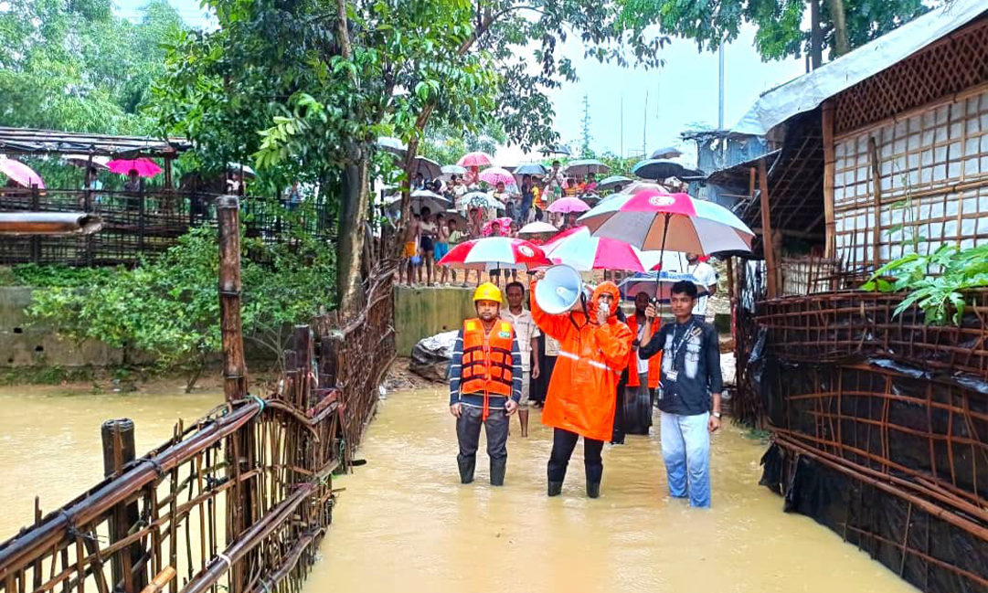 浸水した通路で、オレンジ色の装備を身に着けたボランティアが拡声器で住民を誘導している