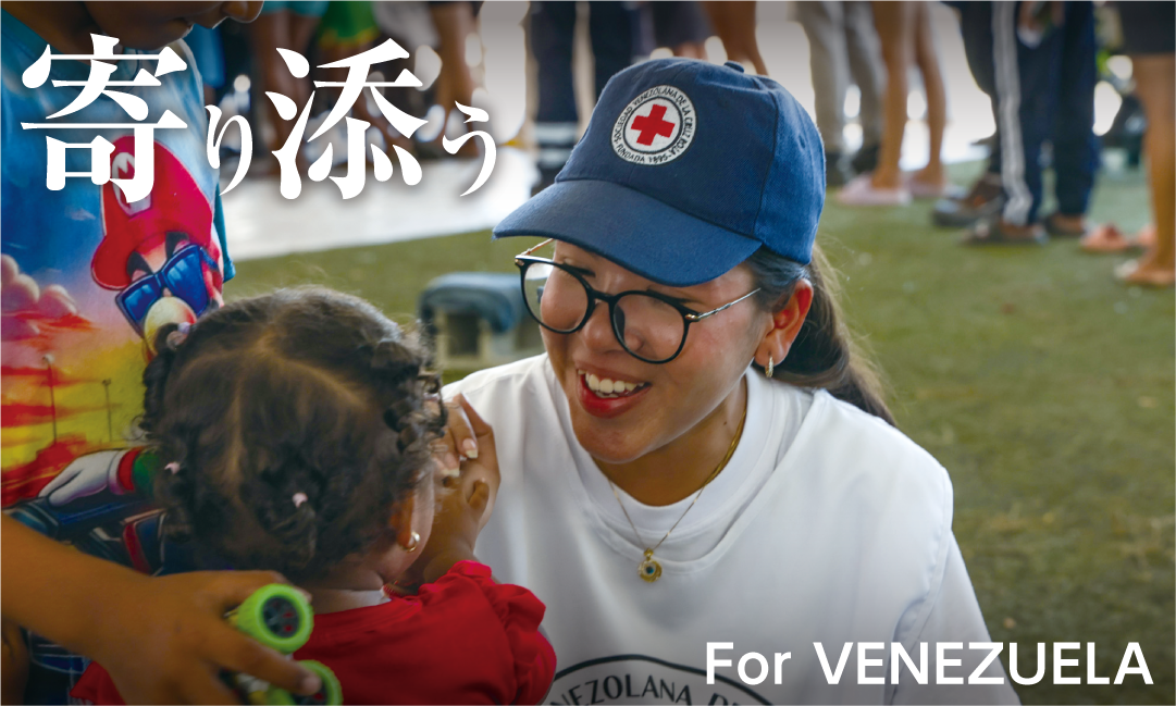 寄り添う For VENEZUELA　赤十字のキャップをかぶったスタッフが子どもに笑顔で寄り添う様子